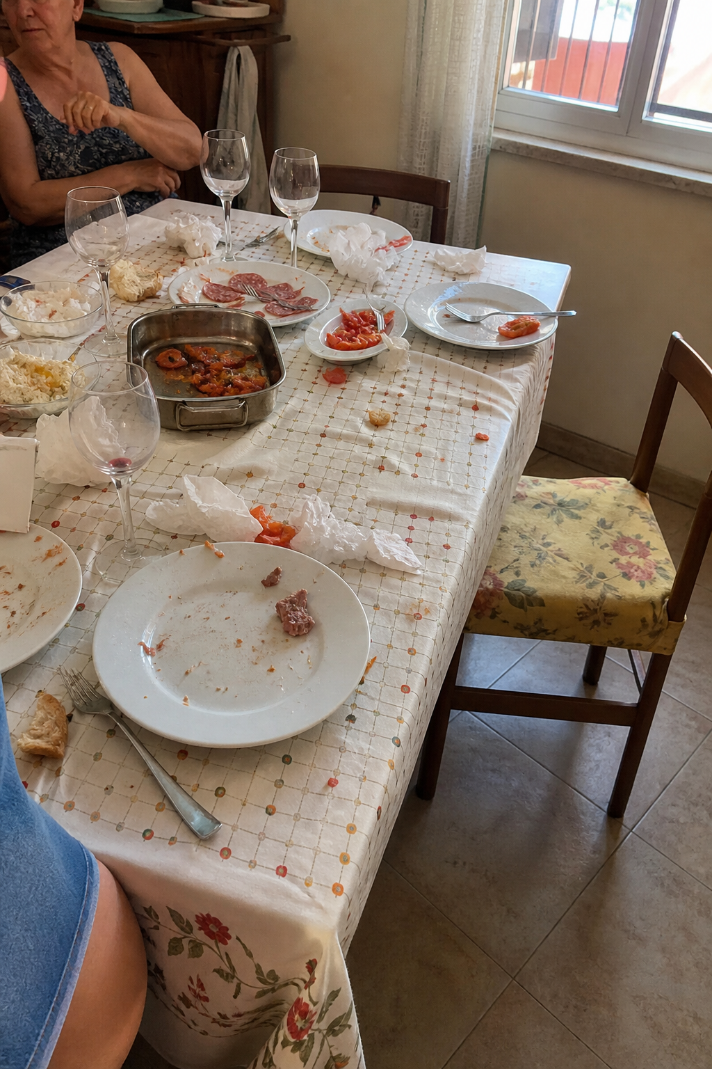 Il tavolo dopo il pranzo. Briciole, un bicchiere, una sedia spostata.